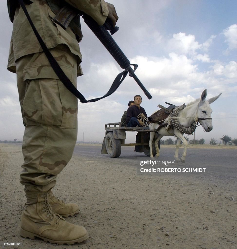 TOPSHOT - Two Iraqi men ride a donkey cart past a US soldier providing security for a US military armored vehicle convoy temporarily parked on the side of a road during a maintenance stop on a highway northeast of Baquba, 07 May 2003. US soldiers from the 2-8 Infantry, 4 Infantry Division moved north in an effort to expand their presence in this region of the country.  AFP PHOTO/Roberto SCHMIDT (Photo by ROBERTO SCHMIDT / AFP) (Photo by ROBERTO SCHMIDT/AFP via Getty Images)