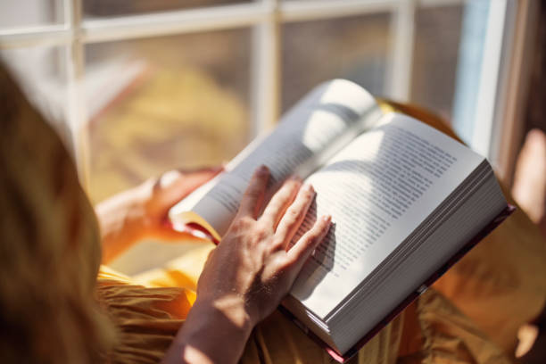 Teenage girl enjoying reading a book on windowsill. Sunny summer day.Shot with Canon R5