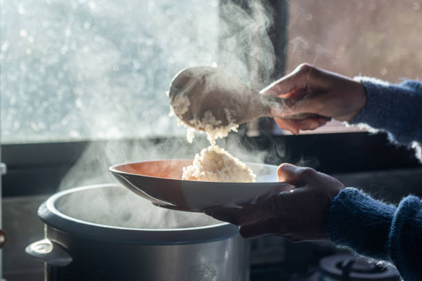 selective focus,soft focus Women hand holding and using wood ladle to scoop steamed rice from electric rice cooker with blur background