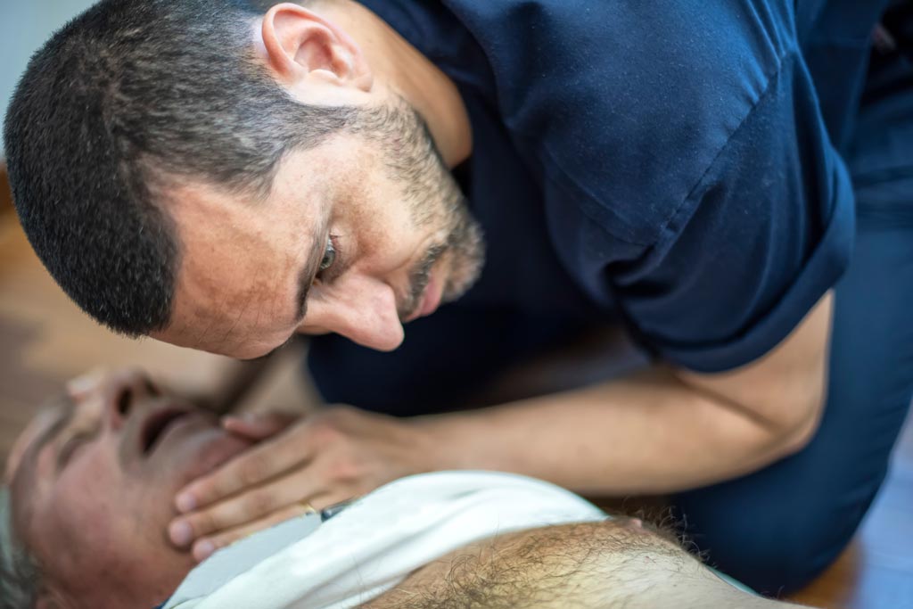 Man checks for breathing in unconscious elderly man experiencing cardiac arrest
