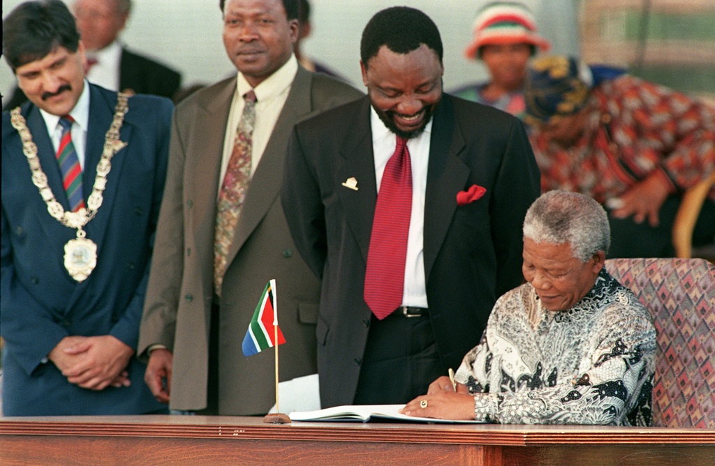 South African President Nelson Mandela (R) signs the country's new constitution while ANC's chief negociator during the drafting process Cyril Ramaphosa looks on, at Sharpville stadium near Vereeniging 10 December 1996. The venue has a double significance : in the same town, in 1902 the Treaty of Vereeniging which ended the Anglo-Boer War was signed and in 1960 police shot dead 69 people during an anti-apartheid demonstration in the township of Sharpville.     AFP PHOTO ADIL BRADLOW / AFP PHOTO / ADIL BRADLOW