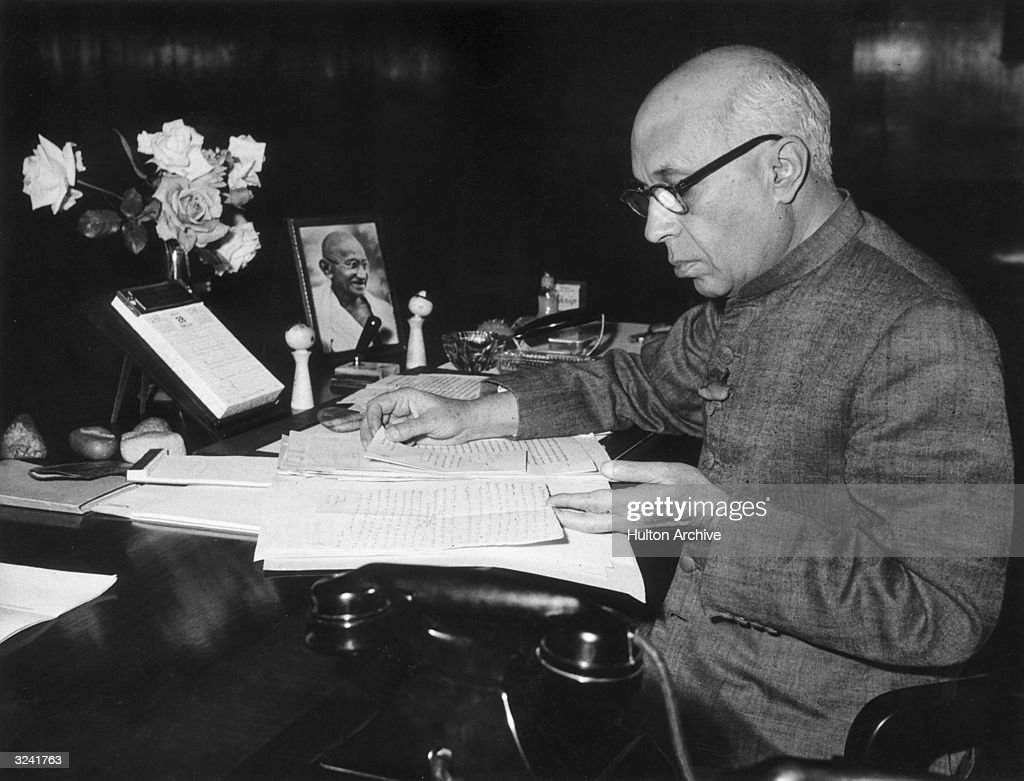 28th February 1958:  Indian Prime Minister Pandit Jawaharlal Nehru (1889 - 1964) reading a budget before presenting it to the Lok Sabha in Parliament, New Delhi, India. A portrait of Gandhi rests on the desk.  (Photo by Hulton Archive/Getty Images)